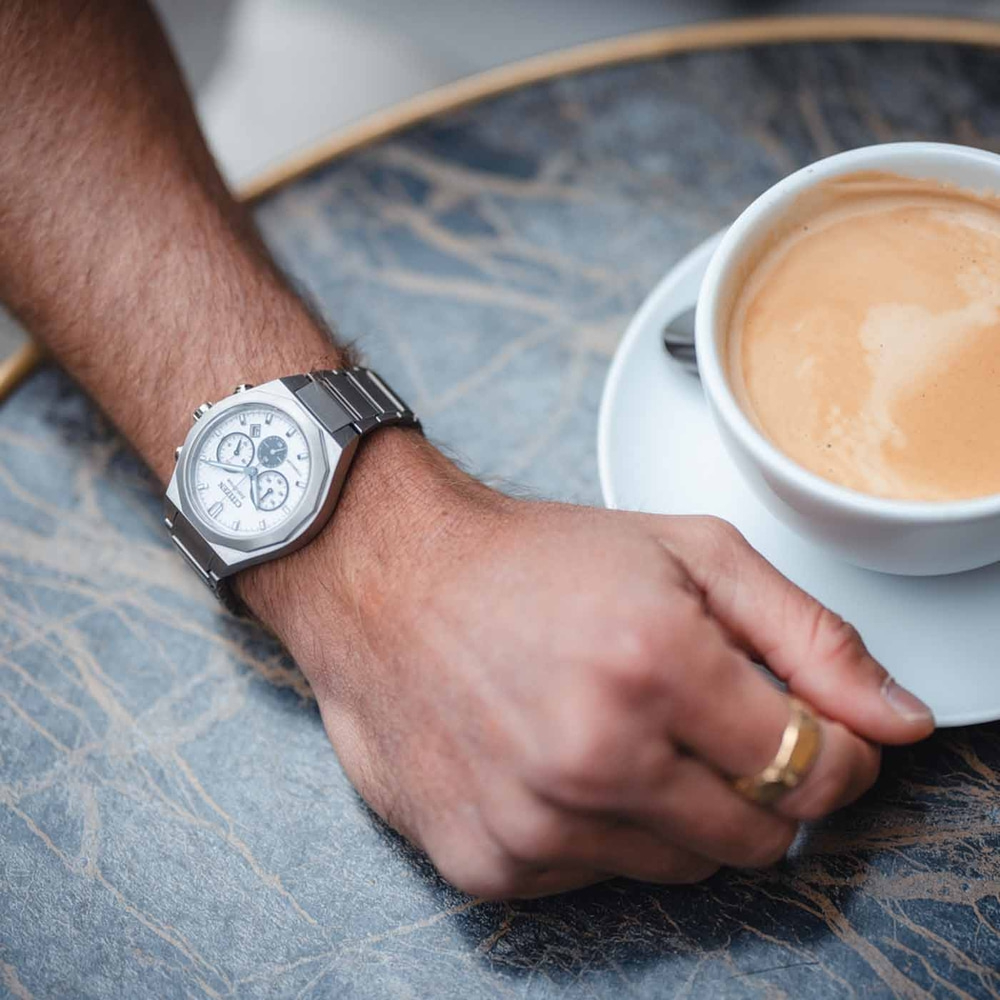 Nahaufnahme einer Armbanduhr und einer Kaffeetasse auf einem Tisch.